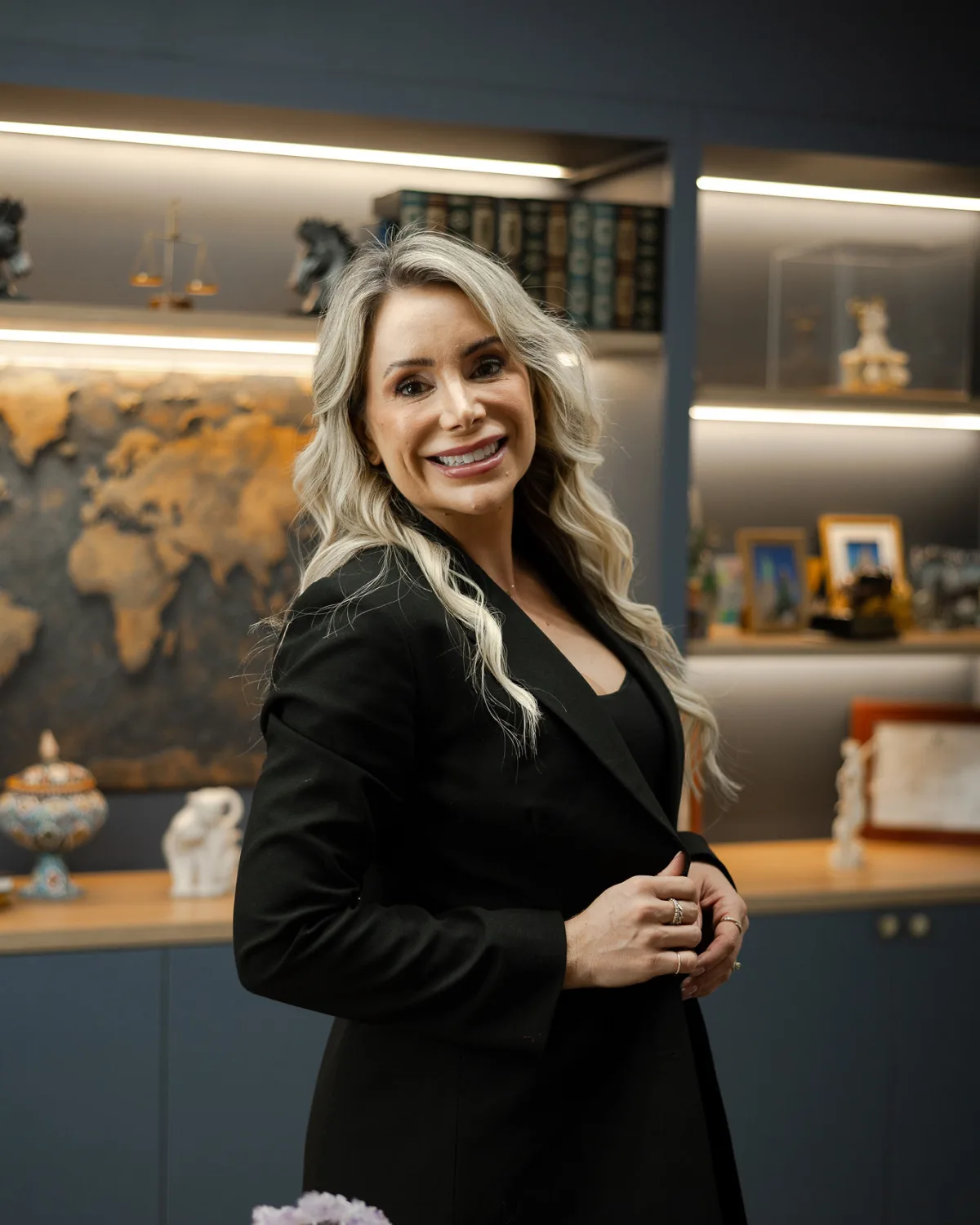 Dra. Fernanda Gehm na sala dela, diante da estante com o mapa-múndi