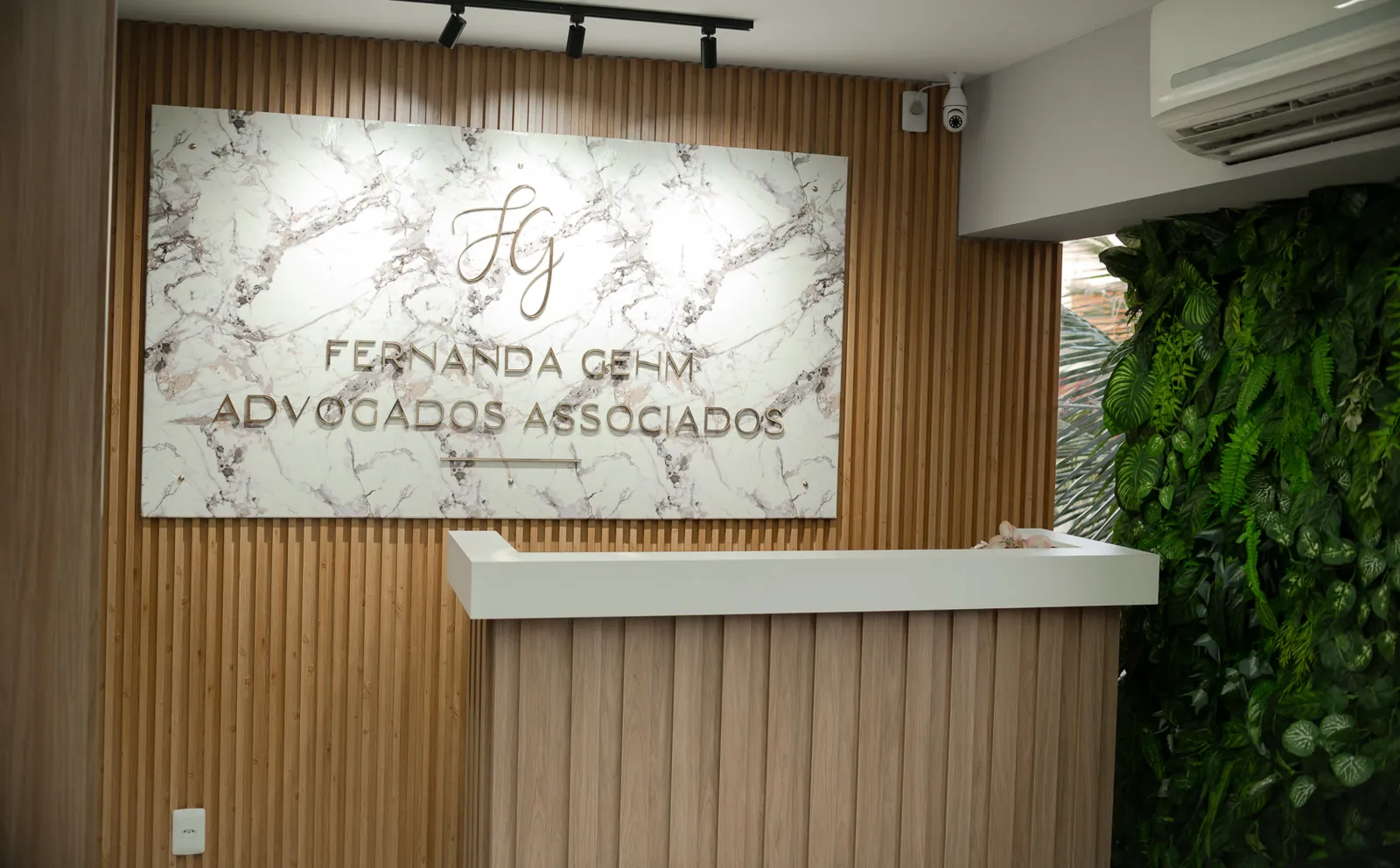 Recepção do escritório, com o logotipo na parede de mármore e a parede de folhagens